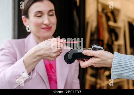 Donna sorridente in giacca rosa a pagamento con la sua carta di credito Foto Stock