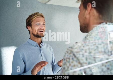 Due giovani uomini d'affari che parlano dietro windowpane Foto Stock
