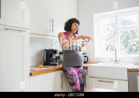 Donna incinta mangiare in cucina Foto Stock