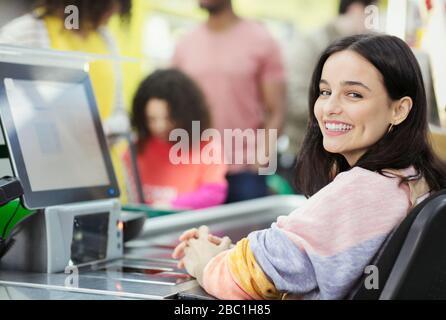 Ritratto sorridente, cassiere donna fiducioso che lavora al supermercato checkout Foto Stock