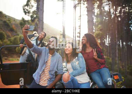 Giovani amici con fotocamera telefono a prendere selfie in jeep nei boschi Foto Stock