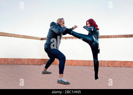 Donna rossa che indossa una tuta in pelle nera che combatte contro l'uomo sul tetto Foto Stock