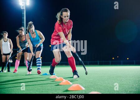 Determinato giovane giocatore di hockey da campo femminile praticando sport trivella sul campo di notte Foto Stock