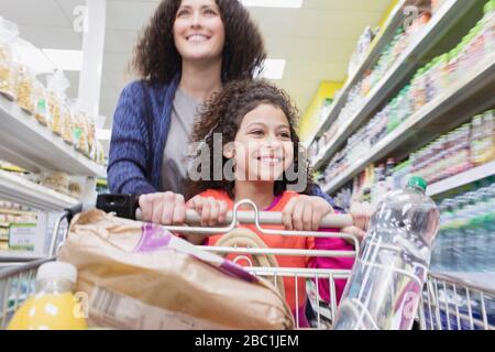 Madre felice e figlia che spingono il carrello nella navata del supermercato Foto Stock
