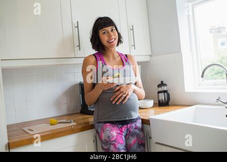 Ritratto donna incinta felice mangiare in cucina Foto Stock