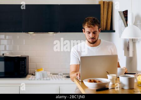 Giovane uomo utilizzando laptop in cucina Foto Stock