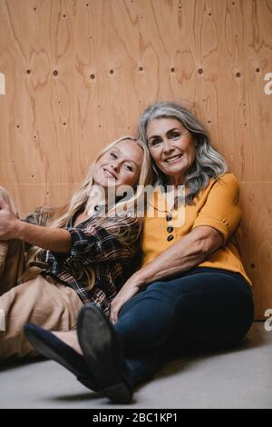 Ritratto di madre sorridente e di figlia adulta seduta sul pavimento Foto Stock