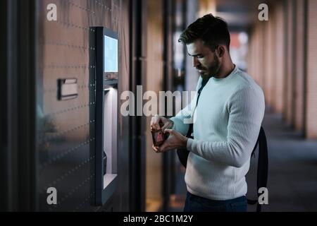 Uomo che ritira denaro in un bancomat della città Foto Stock