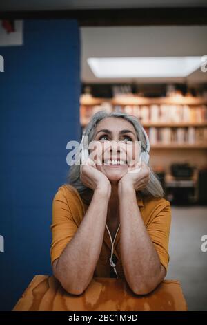 Felice donna dai capelli grigi che ascolta musica con le cuffie Foto Stock