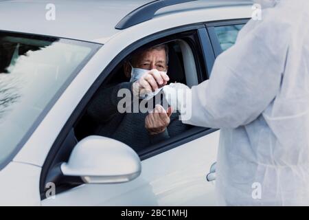 Uomo che indossa indumenti protettivi per controllare l'uomo anziano in auto Foto Stock