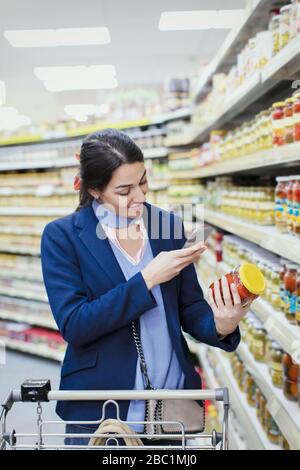 Donna con etichetta scansione smartphone sul vaso in supermercato Foto Stock