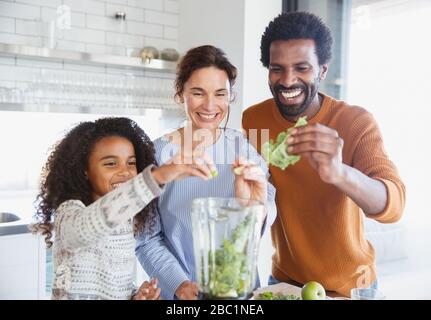 Famiglia multietnica sorridente che fa frullato verde in frullatore in cucina Foto Stock