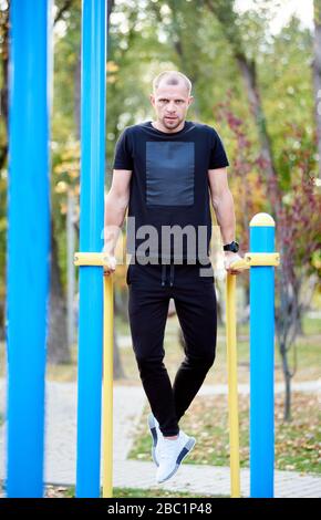 Il vestito nero sportivo a figura intera indossa un abito nero che si sta lavorando sulle barre parallele all'aperto, concentrando il look nella fotocamera. Foto Stock