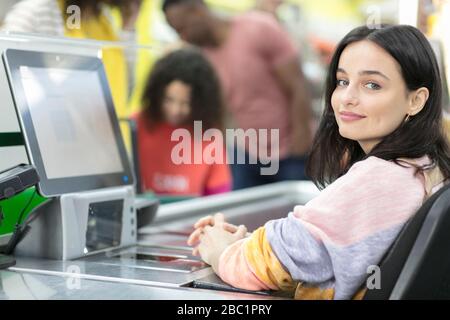 Ritratto sicuro cashier giovane femmina che lavora al checkout in supermercato Foto Stock