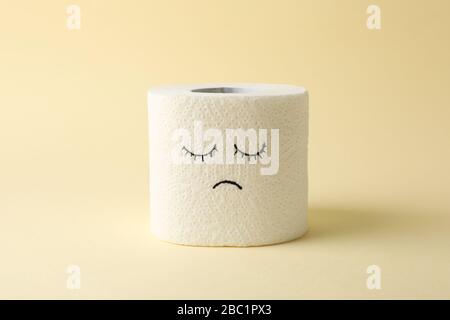 Carta igienica con volto triste su sfondo beige Foto Stock