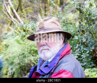 Serio serio poppiero sopportato uomo sano anziano che indossa un cappello e una giacca marroni, fuori che guarda nella macchina fotografica Foto Stock