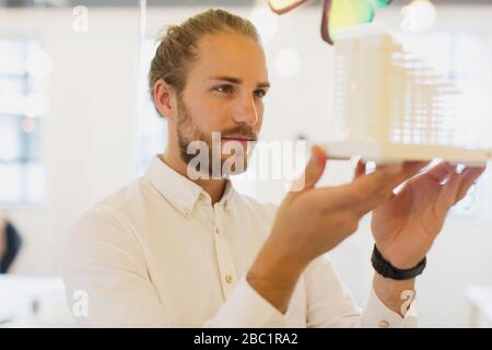 Architetto maschile curioso e concentrato che esamina il modello in ufficio Foto Stock