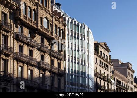 Vista su un edificio moderno tra edifici storici, antichi e tradizionali di Barcellona. È una giornata estiva soleggiata. Foto Stock