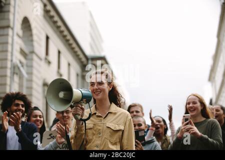 Giovane donna con gruppo di persone in un rally. Donna con un megaphone all'aperto sulla strada durante una protesta. Foto Stock