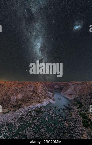 Una maestosa fotografia verticale del cielo notturno con la Via Lattea e le Nuvole Magellaniche nel cielo blu profondo, con vista sul fiume e le montagne alla A Foto Stock