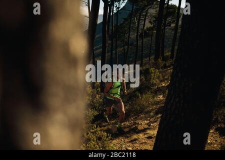 Montare il giovane uomo di indossare abbigliamento sportivo di idratazione pack correndo all'aperto su sentiero roccioso sulla collina. Sentiero di montagna runner praticando sul tracciato sterrato. Foto Stock