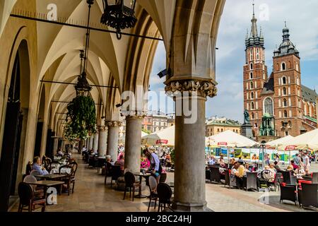 Tavoli da caffè occupati nella Rynek Główny o piazza principale, con vista sulla Basilica di Santa Maria, nel centro di Cracovia, Polonia. Luglio 2017. Foto Stock