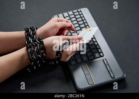 Donna con catena di metallo che tiene la carta di credito sopra la tastiera, concetto di dipendenza di shopping in linea Foto Stock