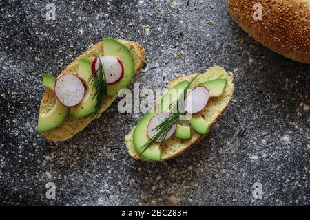 Panini vegani fatti di rotolo di pane di mais con avocado, ravanello e aneto su sfondo nero cosparso di farina Foto Stock