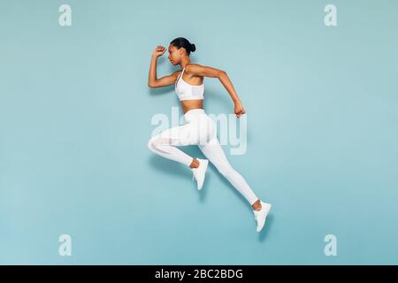 Donna sportiva che corre in studio. Scatto completo di giovane femmina che esercita su backgroud blu. Foto Stock