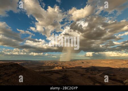 Un suggestivo paesaggio nuvoloso preso al tramonto in una giornata tempestosa in cima all'arido e aspra Fish River Canyon, Namibia, con pioggia e un arcobaleno nel di Foto Stock