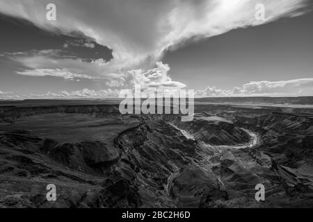 Un paesaggio bianco e nero preso al tramonto in una giornata tempestosa in cima all'arido e aspra Fish River Canyon, Namibia, con la gola e il fiume nel f Foto Stock