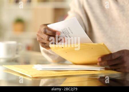 Primo piano di mani nere che aprono una busta imbottita con una lettera su una scrivania a casa Foto Stock