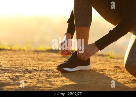 Il closeup della donna runner mani legando scarpe di scarpe a terra al tramonto Foto Stock