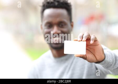 Vista frontale ritratto di un uomo felice nero che mostra vuoto carta di credito mockup nel parco Foto Stock