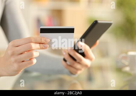 Primo piano di donne mani a pagamento con carta di credito su smartphone su una scrivania a casa Foto Stock