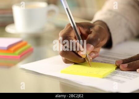 Primo piano di nero mano uomo scrivere promemoria su nota appiccicosa su una scrivania a casa Foto Stock