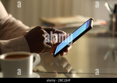 vista laterale primo piano ritratto di un uomo nero mani utilizzando il telefono cellulare su una scrivania di notte a casa o in ufficio Foto Stock