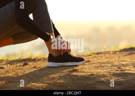 Vista laterale primo piano di corridore donna mani legando scarpe di scarpe a terra al tramonto Foto Stock