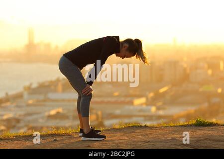 Profilo di un corridore esausto che riposa dopo aver eseguito nella periferia della città al tramonto Foto Stock