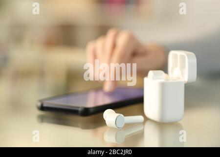 Primo piano della mano della ragazza con gli auricolari che si associano allo smartphone su una scrivania a casa Foto Stock