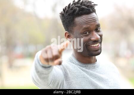 Felice uomo nero che punta alla macchina fotografica in piedi in un parco Foto Stock