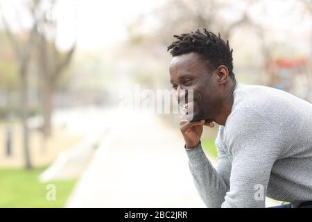 Ritratto di un uomo nero felice che guarda lontano seduto alla panchina del parco Foto Stock