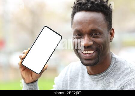 Vista frontale ritratto di un uomo felice nero che mostra smartphone con schermo vuoto nel parco Foto Stock