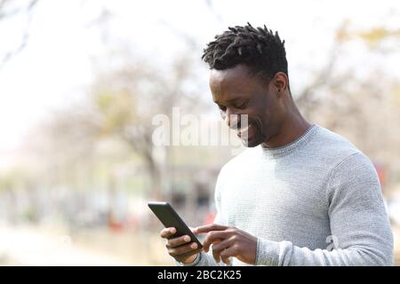 Felice uomo nero utilizzando smartphone a piedi in un parco una giornata di sole Foto Stock