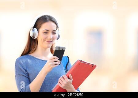 Gli studenti che indossano cuffie wireless ascoltano la musica sul suo smartphone camminando all'aperto Foto Stock
