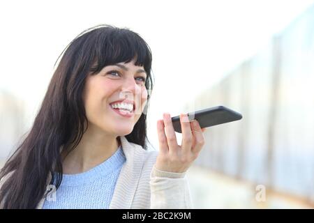 Buona donna che registra il messaggio utilizzando il riconoscimento vocale sullo smartphone in un ponte Foto Stock