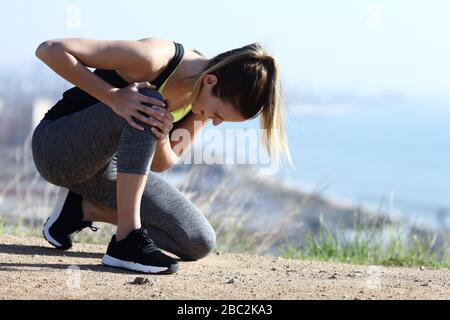 Corridore ferito lamentarsi da solo dolore al ginocchio a terra nella periferia della città Foto Stock