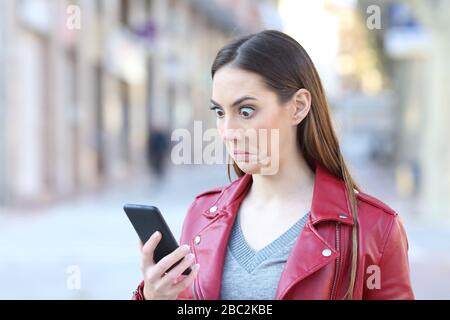 Perplessa donna che controlla le notizie del telefono intelligente in piedi nella strada Foto Stock