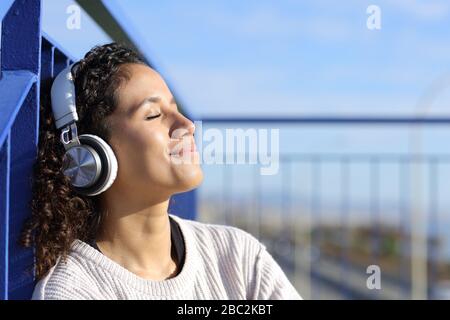 Rilassante ragazza latina ascoltare musica all'aperto seduti sulle scale appoggiandosi in un caldo di ringhiera in una giornata di sole Foto Stock