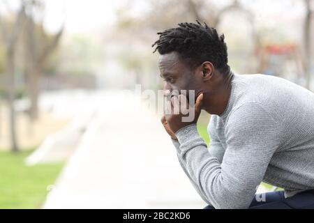 Vista laterale ritratto di un serio uomo nero pensoso che guarda lontano seduto su una panchina del parco Foto Stock